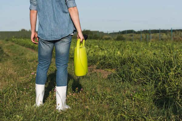 partial view of farmer in white rubber boots standing with yellow watering can in field