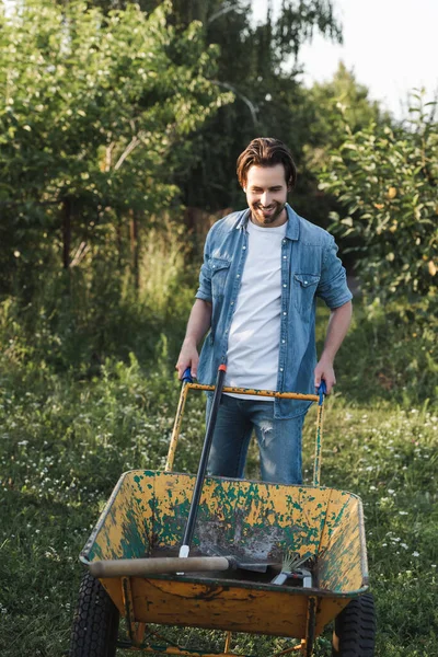 Agricultor Sorridente Roupas Ganga Perto Carrinho Mão Com Ferramentas Jardinagem — Fotografia de Stock