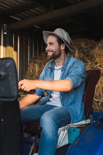 happy farmer in brim hat looking away while sitting on tractor
