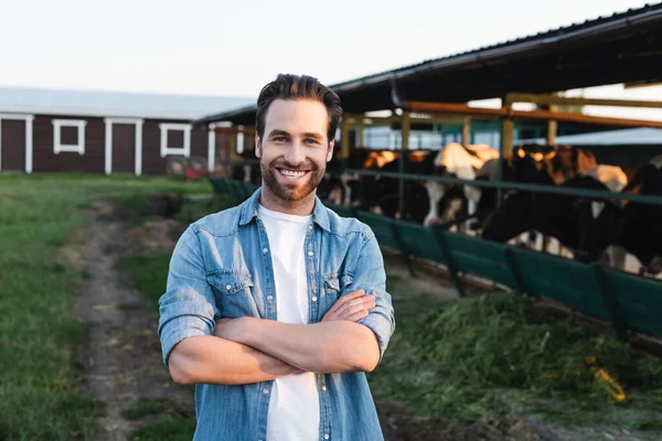 農場の牛小屋の近くで両腕を組んで立っている幸せな農家 — ストック写真