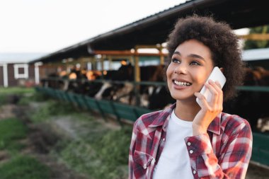 Neşeli Afrikalı Amerikalı kadın, çiftlikte akıllı telefondan konuşurken gözlerini kaçırıyor.
