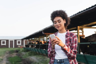 Genç Afrikalı Amerikalı kadın cep telefonu kullanıyor. Bulanık inek ahırının yanında.