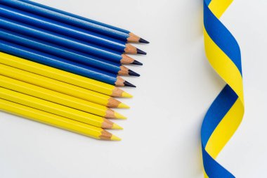 Beyaz arkaplanda renkli kalemlerin yanında sarı ve mavi kurdelelerin üst görünümü 