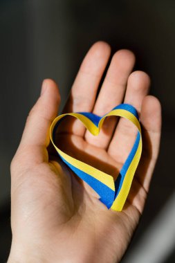 Kırpılmış mavi ve sarı kurdele kalp şeklinde koyu gri arka planda erkek eli 