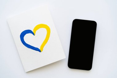 Beyaz zemin üzerinde mavi ve sarı kalp işareti olan beyaz ekranlı akıllı telefonun üst görünümü 
