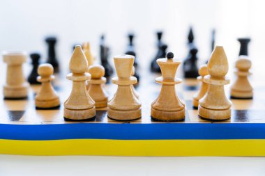 Satranç tahtasının yakınındaki mavi ve sarı kurdelenin beyaz arkaplandaki satranç tahtasını kapat 