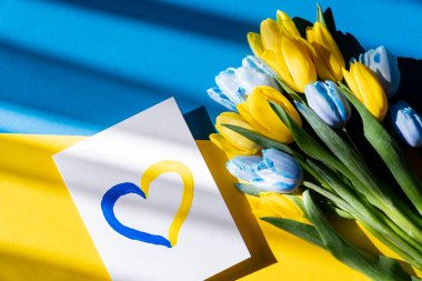 Ukrayna bayrağında mavi ve sarı lalelerin yanında boyalı kalp işareti olan kartın üst görüntüsü