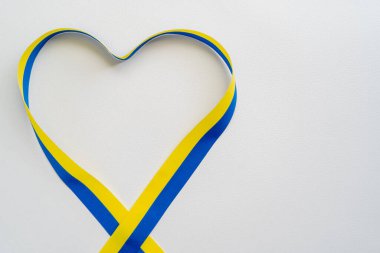 Mavi ve sarı kurdelenin beyaz zemin üzerinde kalp şeklinde ve kopya alanı ile üst görünümü