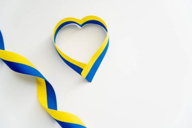 Beyaz arkaplanda kalp sembolü şeklinde mavi ve sarı kurdelelerin üst görünümü 