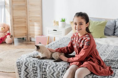 Mutlu kız yatak odasında kediyi okşarken kameraya bakıyor.