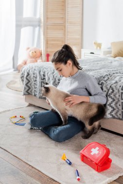 Oyuncak tıbbi aletlerin yanında kediyi okşayan kızın geniş açılı görüntüsü