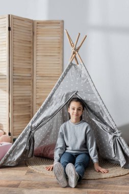 Wingwam 'da yerde oturan mutlu kızın uzun manzarası.