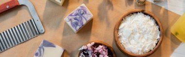 Top view of handmade soap bars near flakes and flowers on craft paper, banner  clipart
