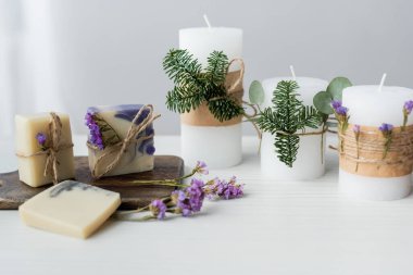 Gri arkaplanda, mumların yanında kesme tahtasında çiçekler olan sabun kalıpları. 