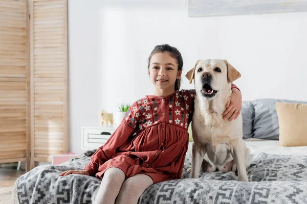 Menina Morena Feliz Abraçando Labrador Sorrindo Para Câmera Enquanto Sentado — Fotografia de Stock