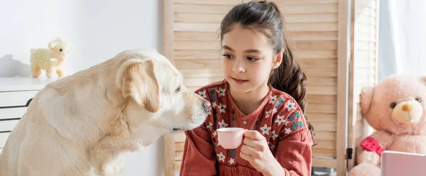 おもちゃのカップを持っている女の子の近くの黄色のラブラドールバナー — ストック写真