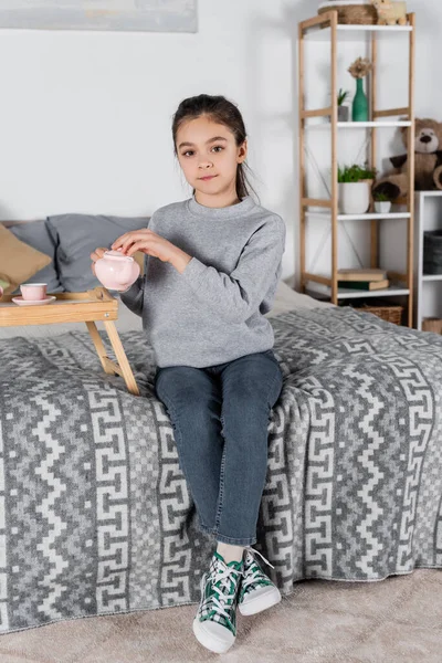 Visão Comprimento Total Menina Sentada Cama Com Bule Brinquedo Olhando — Fotografia de Stock