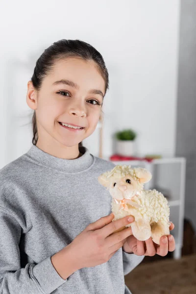 Lächelndes Mädchen Zeigt Spielzeuglamm Und Blickt Die Kamera — Stockfoto