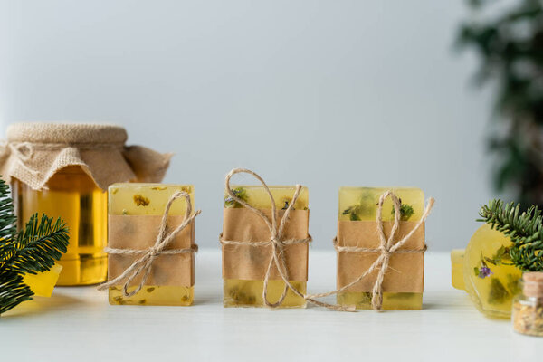 Handmade soap with twine near pine branches and blurred honey on table 
