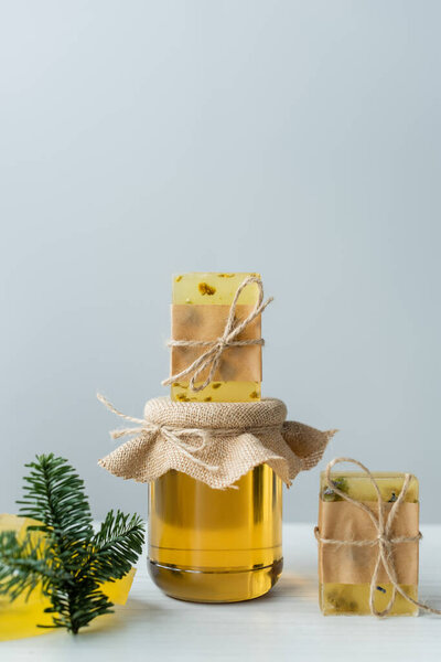 Handmade soap on jar with honey near spruce branch on grey background 