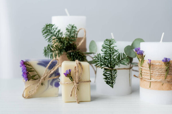 Craft soap bars near candles with spruce branches on grey background 
