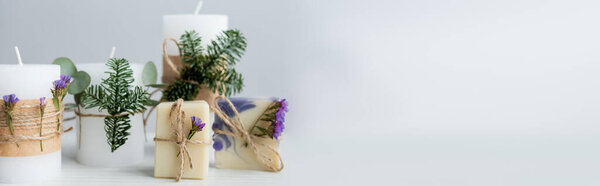 Handmade soap with flowers near candles with pine branches on grey background, banner 