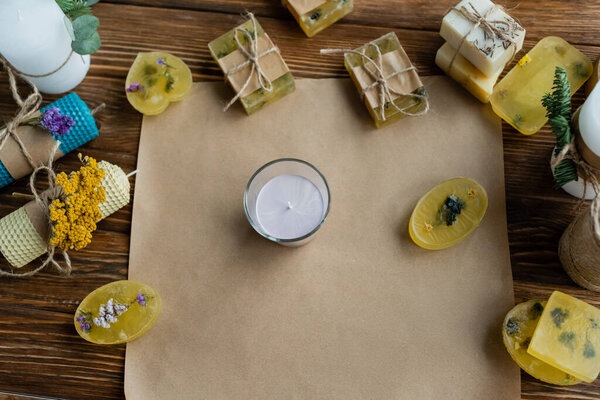 Top view of handmade candles and soap bars on craft paper on wooden surface 