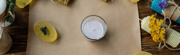 Top view of candle in glass near soap on craft paper on wooden surface, banner 