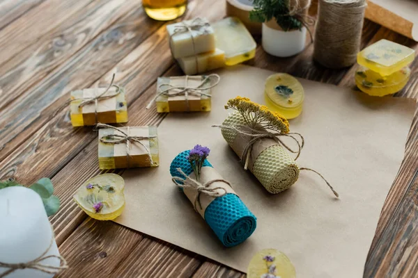 High angle view of handmade candles with flowers on craft paper near soap on wooden surface