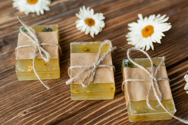 Close up view of handmade soap bards near blurred dry chamomile flowers on wooden surface 