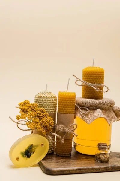 Yellow handmade candles, soap and jar with honey on cutting board on beige background