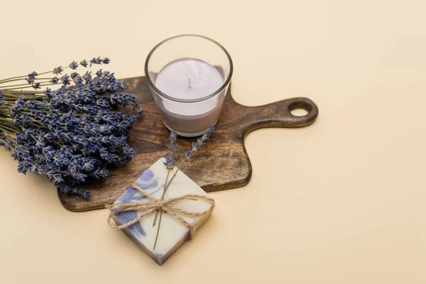 Top view of lavender near handmade soap and candle on cutting board on beige background 