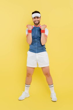 Sarı arka planda dambıllarla çalışan mutlu sporcu. 