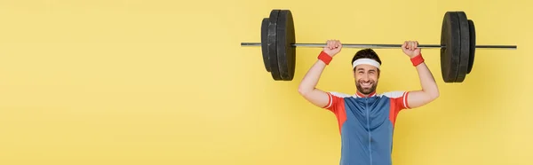Young Sportsman Lifting Barbell Looking Camera Isolated Yellow Banner — Stock Photo, Image