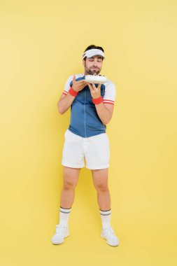 Tam boy genç sporcu sarı arka planda lezzetli pastaya bakıyor. 
