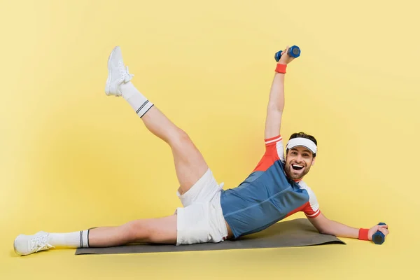 Esportista Positivo Segurando Halteres Enquanto Treinava Tapete Fitness Fundo Amarelo — Fotografia de Stock