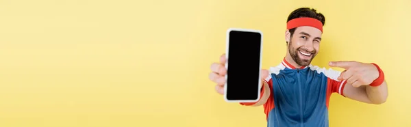 Позитивний Спортсмен Підморгує Вказує Мобільний Телефон Ізольовано Жовтому Банер — стокове фото
