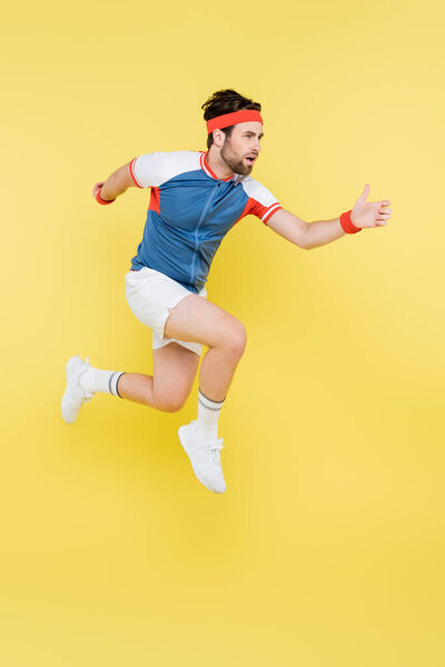 Bearded sportsman jumping and looking away isolated on yellow 