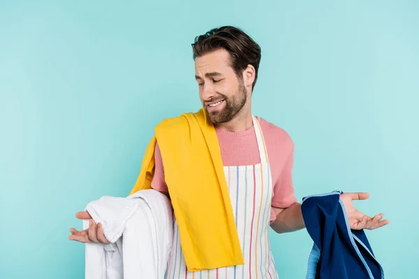 Verwirrter Mann Schürze Blickt Auf Kleidung Isoliert Auf Blauem Grund — Stockfoto