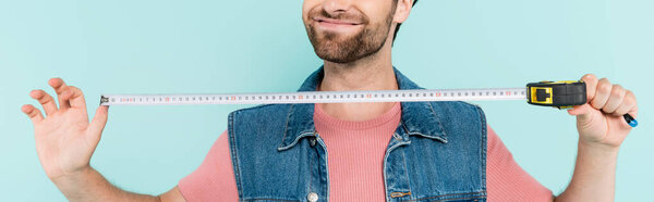 Cropped view of positive man holding tape measure isolated on blue, banner 