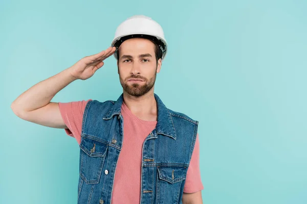 Ung Man Hardhat Salutering Och Tittar Kameran Isolerad Blå — Stockfoto