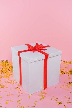 Pembe arka planda konfeti yakınında büyük bir hediye kutusu. 