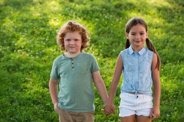 happy brother and sister holding hands and looking at camera outdoors clipart