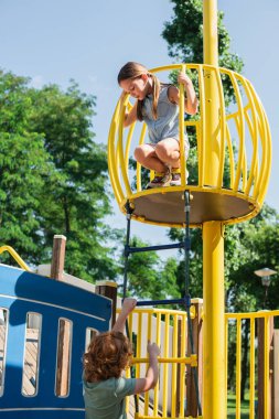 Çocuk lunaparktaki yüksek kulede, kız kardeşinin altında ip merdivene tırmanıyor.