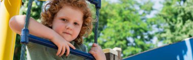 boy looking at camera from rope ladder in amusement park, banner clipart