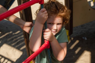 curly boy near rope ladder and mothers hand in amusement park clipart