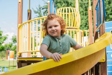 pleased boy looking at camera from slide on playground clipart