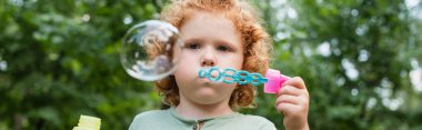 curly child blowing soap bubble outdoors, banner clipart
