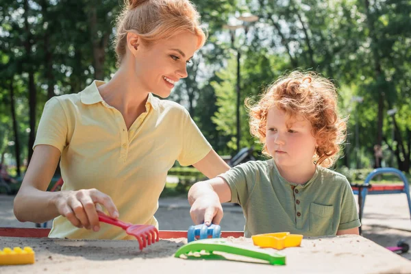 Curly Boy Playing Toy Rakes Sand Cheerful Mother — Stock Photo, Image