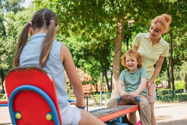 Happy Mom Standing Children Riding Seesaw Playground — Stock Photo, Image